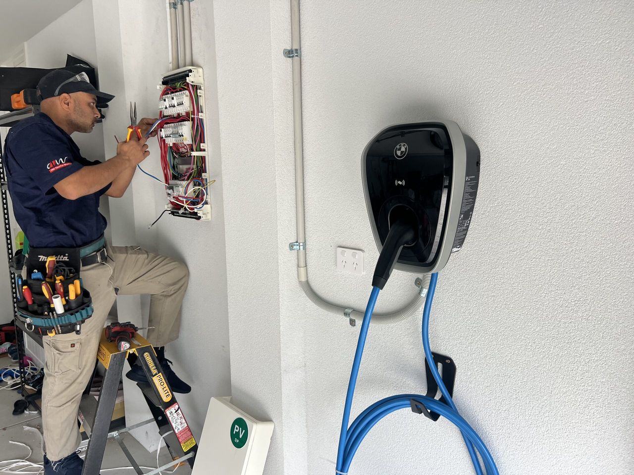 Electrician wiring a distribution board beside a newly fitted AC wallbox charger